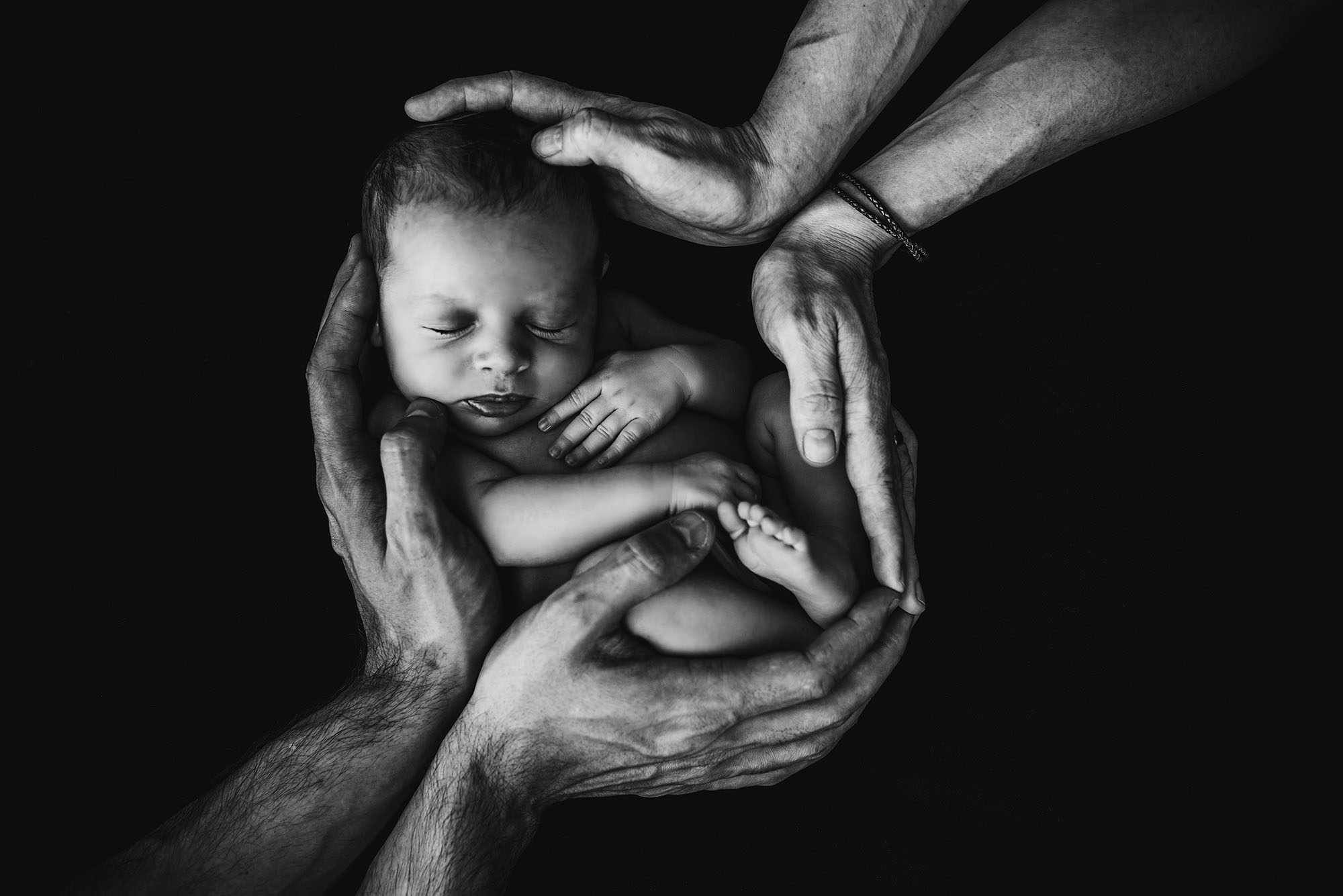 Newborn baby cradled by family's hands in a protective embrace, symbolizing perinatal care and safety.