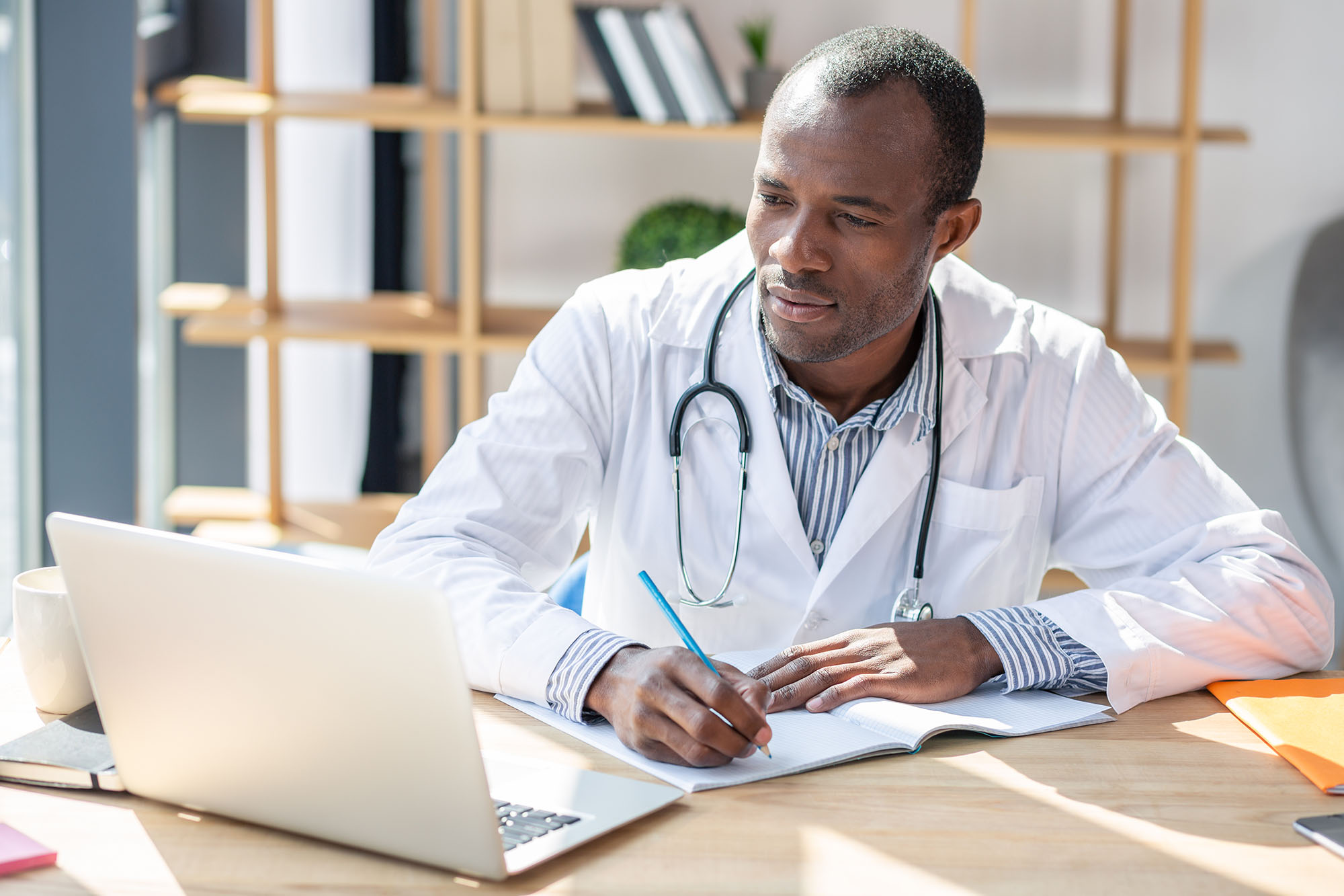 Perinatal care specialist in modern office setting, reviewing medical records on laptop and taking notes